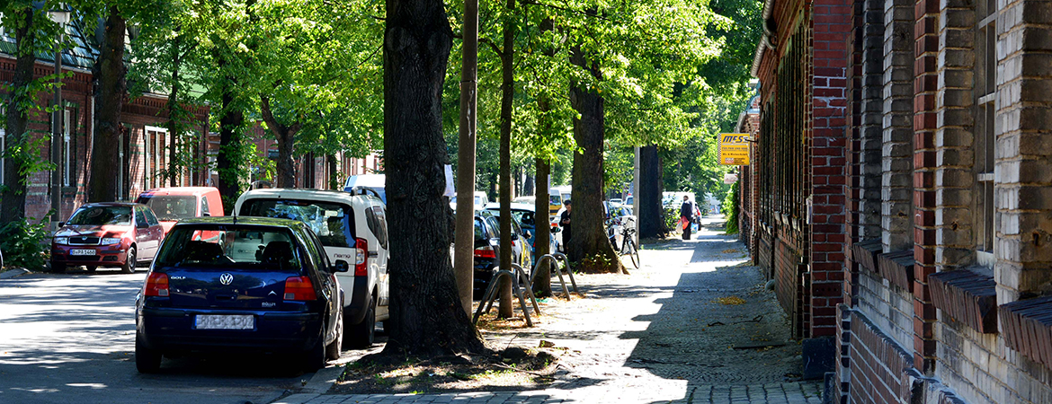 Straße mit Bäumen, Parkende Autos, eingeschossige Backsteingebäude