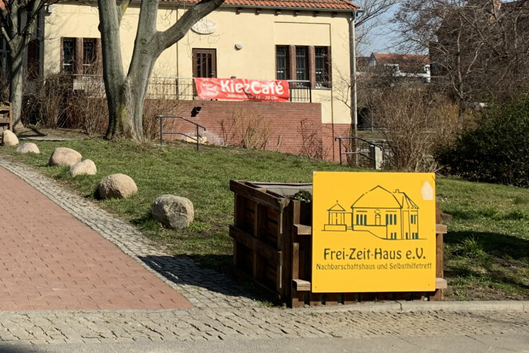 Symbolbild Soziales, Schild mit "Frei-Zeit-Haus e.V." und Eingang zum Gebäude, im Hintergrund Plakat mit Aufschrift "Kiez-Café"